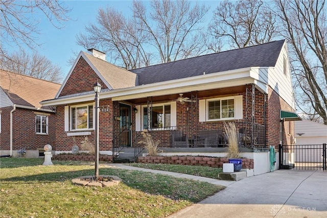 view of front facade featuring a shingled roof, a chimney, covered porch, a front lawn, and brick siding