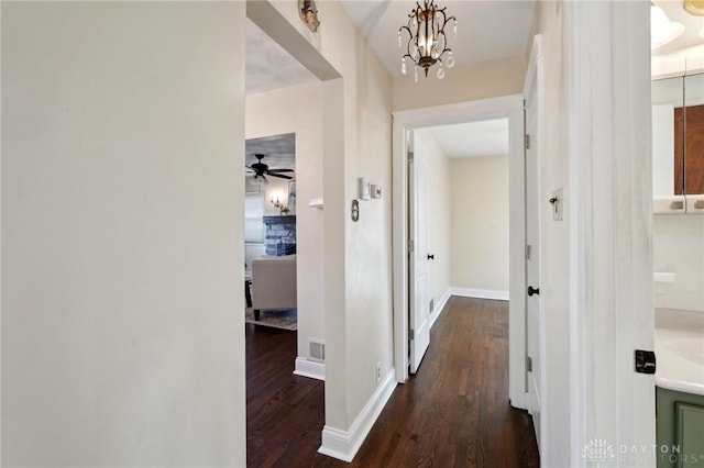 corridor with dark wood-style floors, a notable chandelier, visible vents, and baseboards