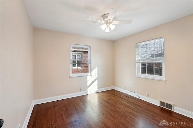 spare room with a ceiling fan, visible vents, baseboards, and wood finished floors