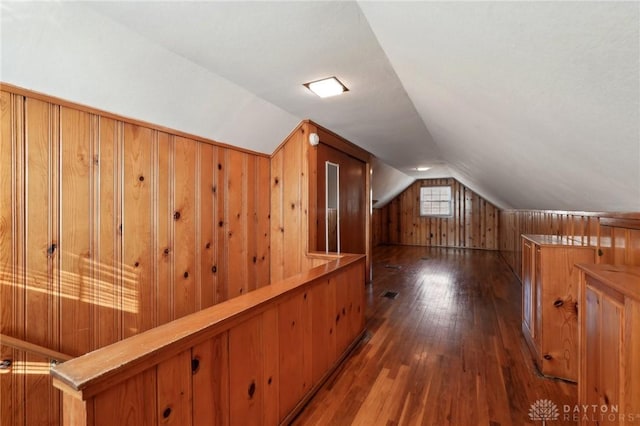 bonus room with lofted ceiling, wood walls, visible vents, and dark wood finished floors