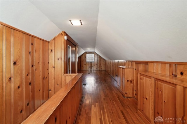 additional living space featuring vaulted ceiling, dark wood-type flooring, and wooden walls