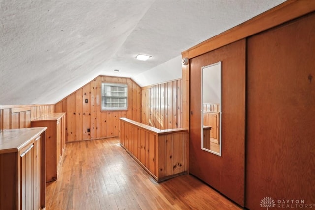 bonus room with wooden walls, lofted ceiling, a textured ceiling, and light wood finished floors