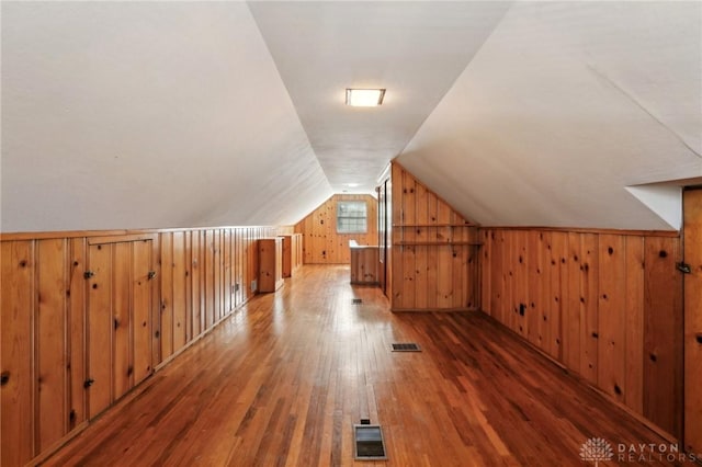 bonus room featuring dark wood-style floors, visible vents, vaulted ceiling, and wooden walls