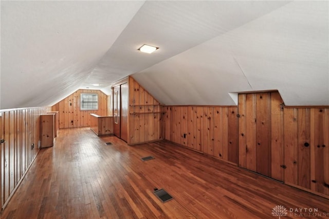 additional living space featuring vaulted ceiling, dark wood-style flooring, visible vents, and wooden walls