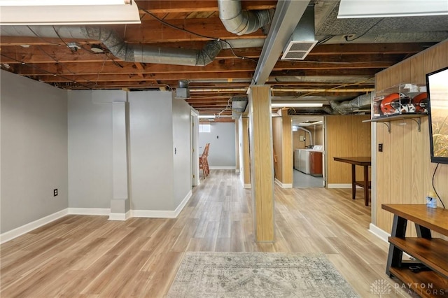 below grade area with light wood-type flooring, washer and dryer, visible vents, and baseboards