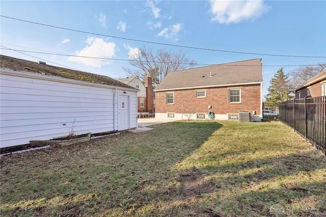 rear view of house with central air condition unit, brick siding, a lawn, and fence