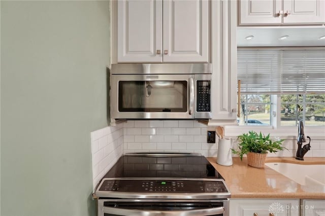 kitchen with stainless steel appliances, a sink, white cabinetry, light countertops, and decorative backsplash