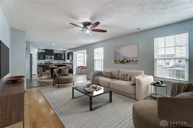 living area featuring visible vents, ceiling fan, a textured ceiling, and light wood finished floors