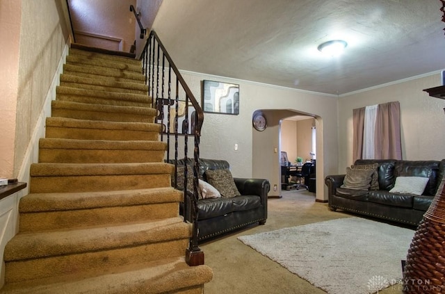 carpeted living area with a textured wall, arched walkways, crown molding, and stairway