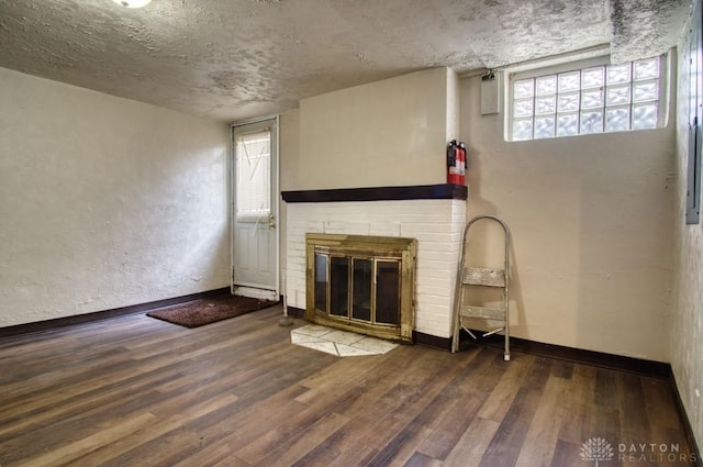 unfurnished living room featuring a textured wall, a fireplace, wood finished floors, and baseboards