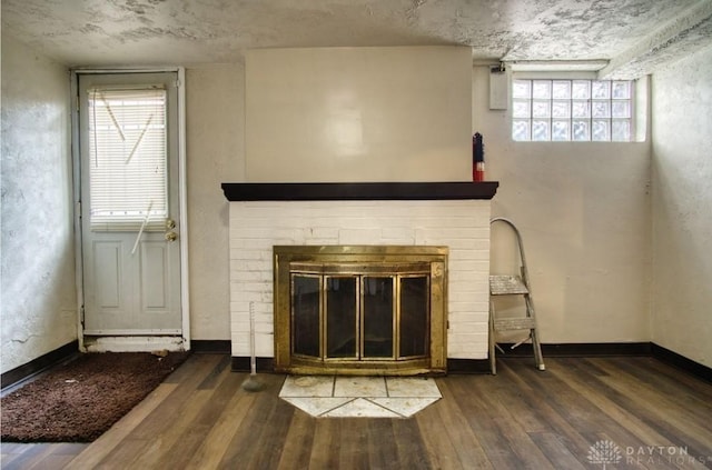 unfurnished living room featuring baseboards, wood-type flooring, and a brick fireplace