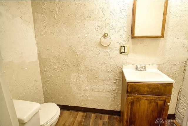 bathroom with toilet, a textured wall, wood finished floors, and vanity