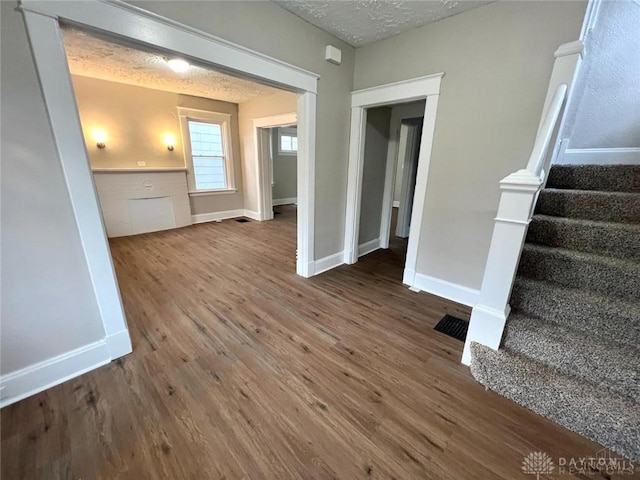 interior space with a wainscoted wall, visible vents, a textured ceiling, wood finished floors, and stairs