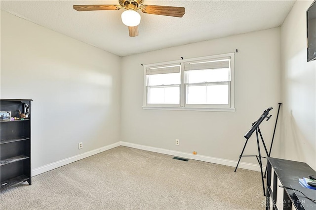 carpeted empty room featuring a textured ceiling, visible vents, a ceiling fan, and baseboards