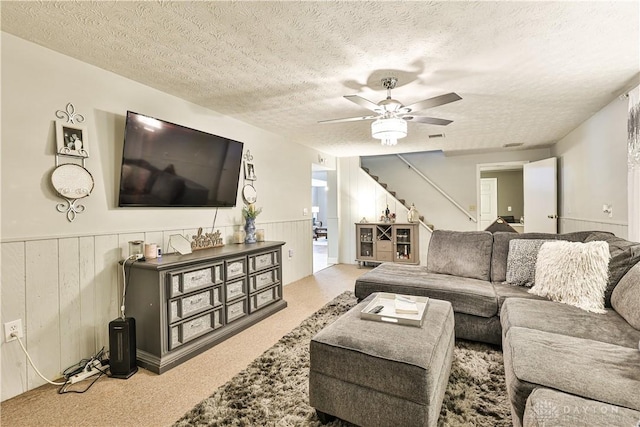 carpeted living area featuring stairway, a textured ceiling, a wainscoted wall, and a ceiling fan