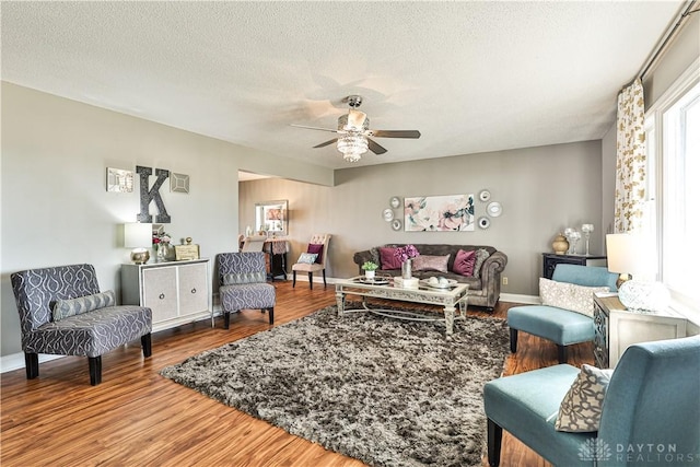living room with baseboards, a ceiling fan, wood finished floors, and a textured ceiling