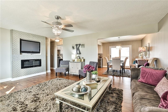 living room with wood finished floors, baseboards, a fireplace, a textured ceiling, and ceiling fan