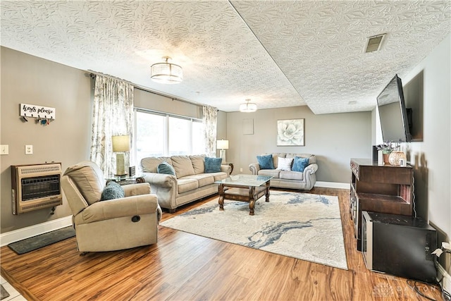 living area with a textured ceiling, baseboards, visible vents, heating unit, and wood finished floors