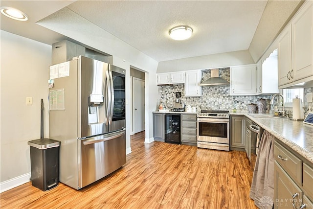 kitchen with wall chimney range hood, a sink, beverage cooler, light wood-style floors, and appliances with stainless steel finishes