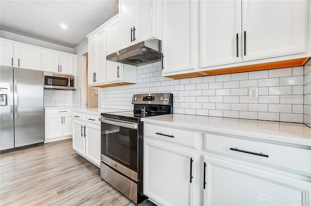 kitchen featuring under cabinet range hood, white cabinets, light countertops, appliances with stainless steel finishes, and light wood-type flooring