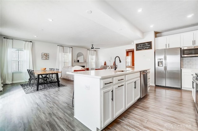 kitchen featuring stainless steel appliances, a sink, open floor plan, light countertops, and a center island with sink