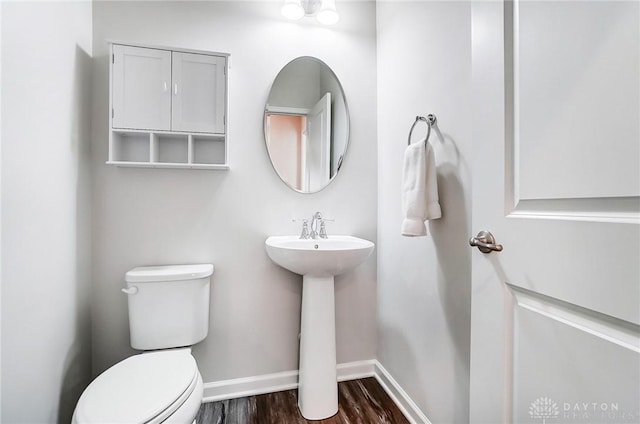 half bathroom with a sink, wood finished floors, toilet, and baseboards