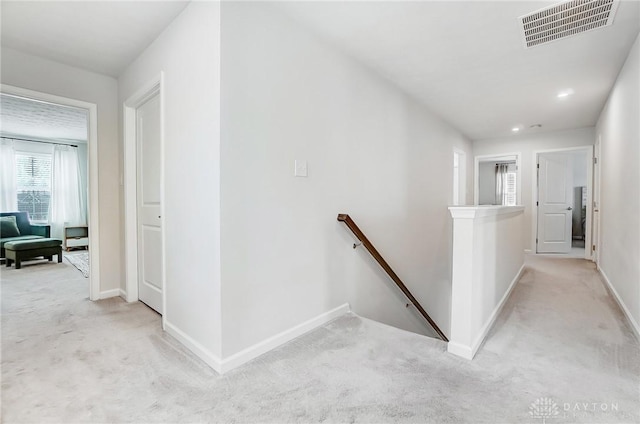 hall featuring light carpet, baseboards, visible vents, and an upstairs landing