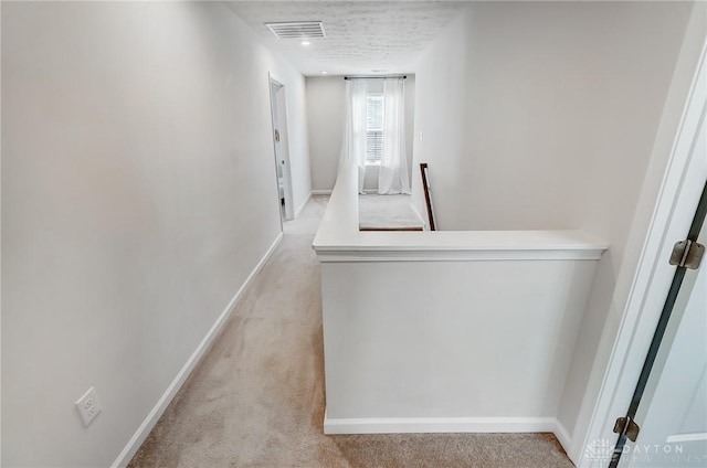 corridor with light carpet, visible vents, and baseboards