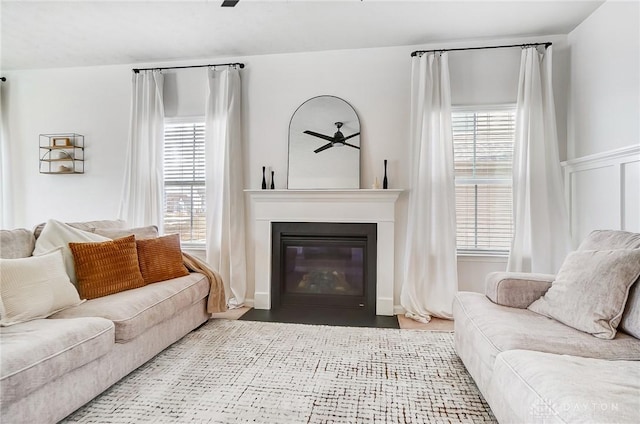 living room with a glass covered fireplace, a ceiling fan, and a healthy amount of sunlight