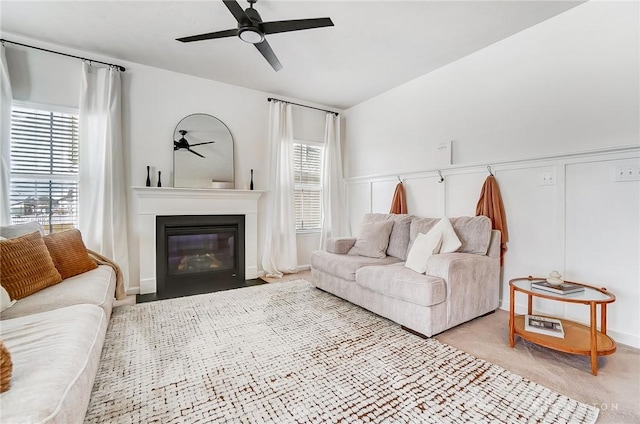 living area with light carpet, a fireplace with flush hearth, a wealth of natural light, and a ceiling fan