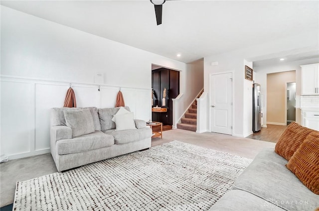 living room featuring wainscoting, light colored carpet, stairs, a decorative wall, and recessed lighting