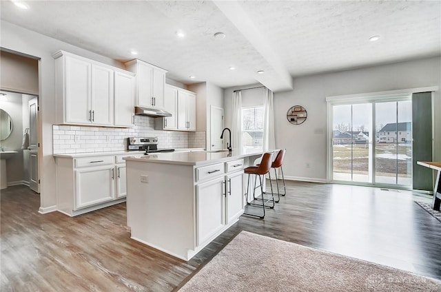 kitchen featuring white cabinets, an island with sink, light countertops, stainless steel range with electric cooktop, and under cabinet range hood