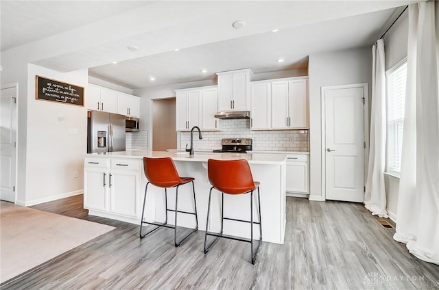 kitchen with an island with sink, stainless steel appliances, light countertops, white cabinetry, and a sink