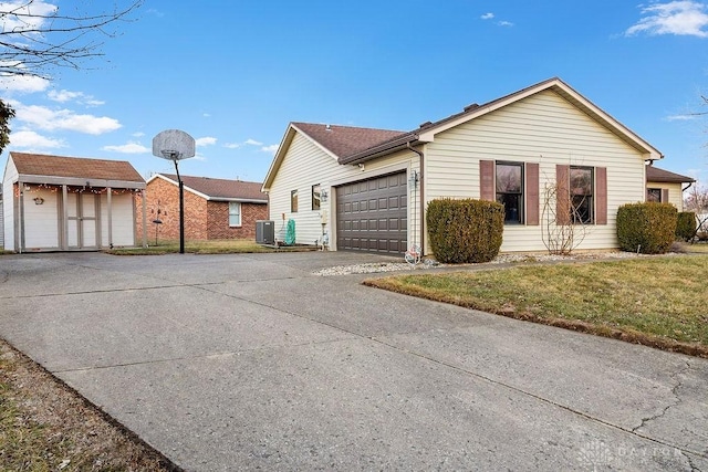 view of front of home with an outbuilding, concrete driveway, an attached garage, central AC, and a front lawn