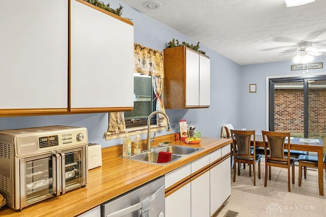 kitchen featuring light countertops, stainless steel dishwasher, white cabinetry, a sink, and a textured ceiling