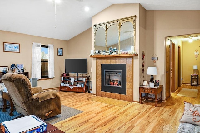 living area featuring lofted ceiling, radiator heating unit, a tiled fireplace, wood finished floors, and baseboards