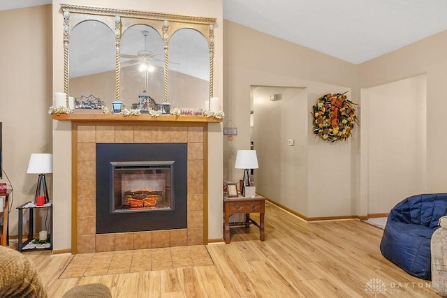 interior space featuring lofted ceiling, baseboards, a tiled fireplace, and wood finished floors