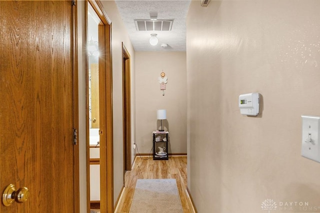 corridor featuring a textured ceiling, light wood finished floors, visible vents, and baseboards