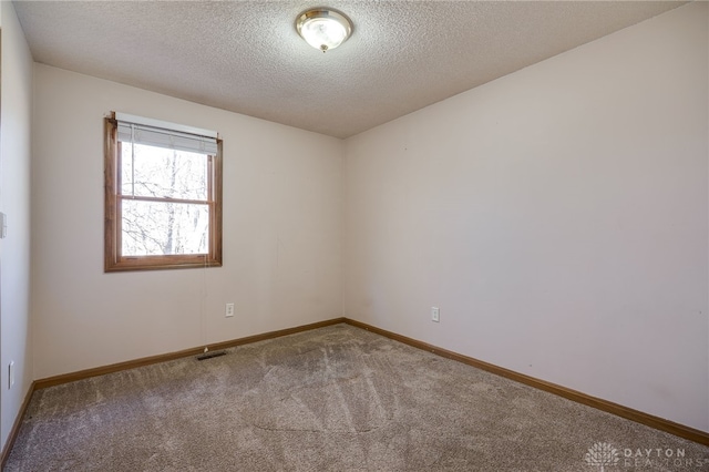 carpeted spare room with a textured ceiling, visible vents, and baseboards