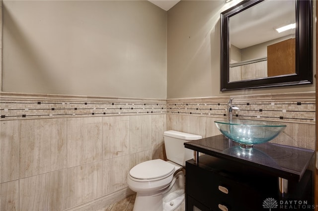 bathroom with toilet, wainscoting, tile walls, and vanity