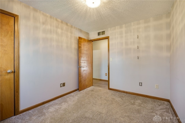 spare room featuring baseboards, visible vents, a textured ceiling, and carpet flooring