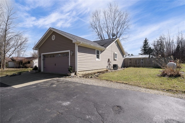 view of home's exterior featuring aphalt driveway, central AC unit, an attached garage, fence, and a yard