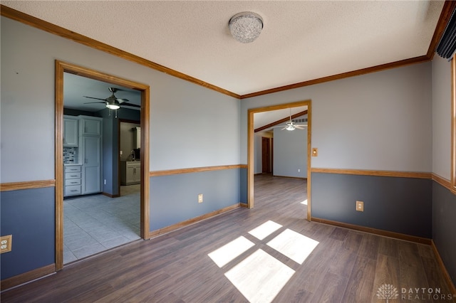 spare room with a textured ceiling, wood finished floors, a ceiling fan, baseboards, and crown molding