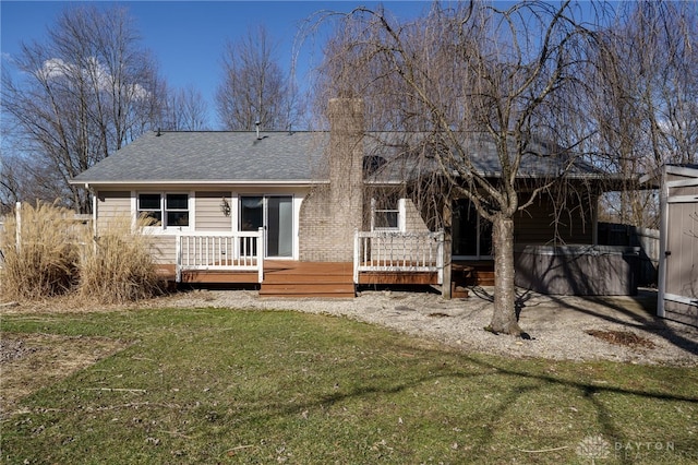 back of property with a yard, a shingled roof, a wooden deck, and a hot tub