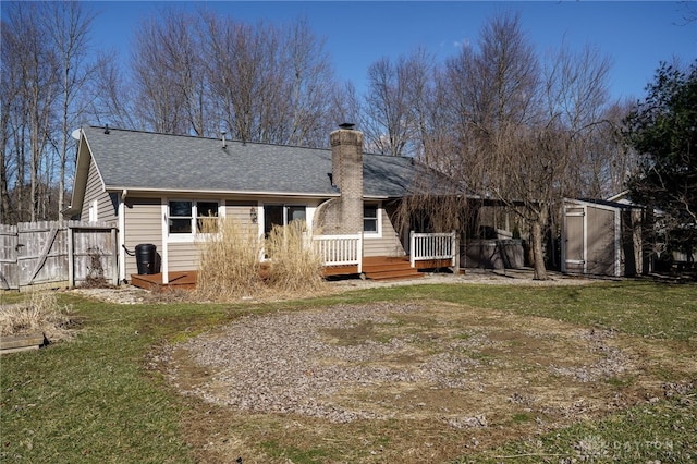 rear view of property with a deck, an outbuilding, a storage shed, fence, and a chimney