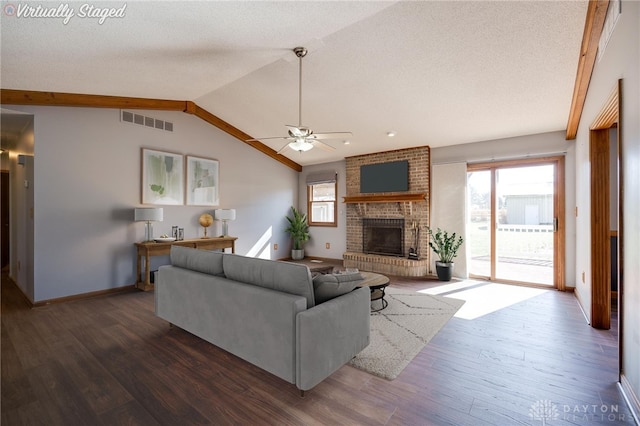 living room featuring lofted ceiling, a brick fireplace, wood finished floors, and visible vents