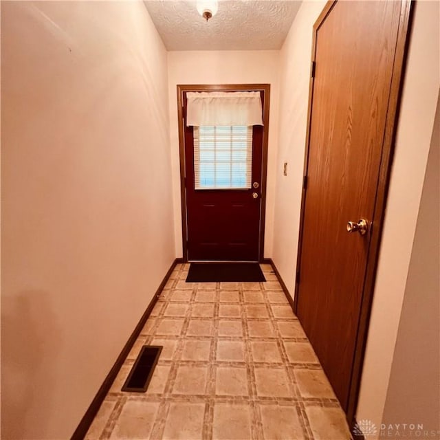 doorway with light floors, baseboards, visible vents, and a textured ceiling