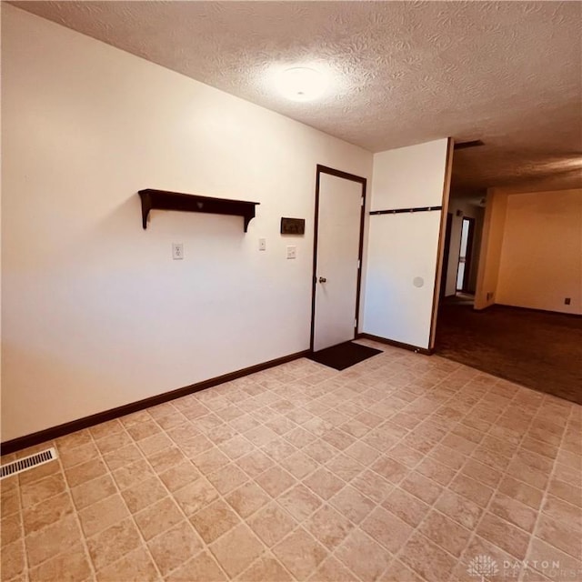 empty room featuring a textured ceiling, light floors, visible vents, and baseboards