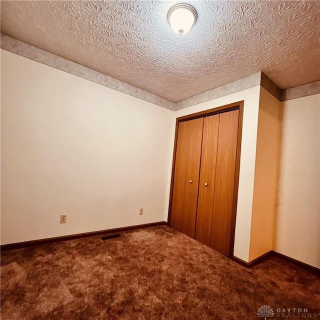 unfurnished bedroom featuring carpet, a closet, visible vents, a textured ceiling, and baseboards