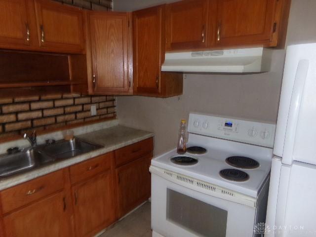 kitchen with white appliances, brown cabinets, light countertops, under cabinet range hood, and a sink